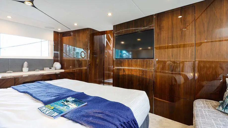 Luxurious bedroom featuring a double bed with blue throw, wooden cabinetry, TV, and natural light through large windows.